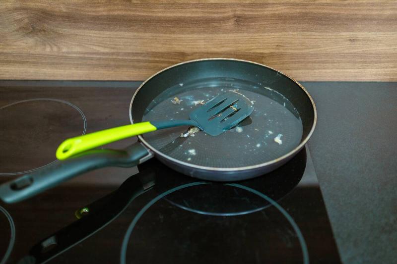 Dirty frying pan with plastic spatula on a stove. 