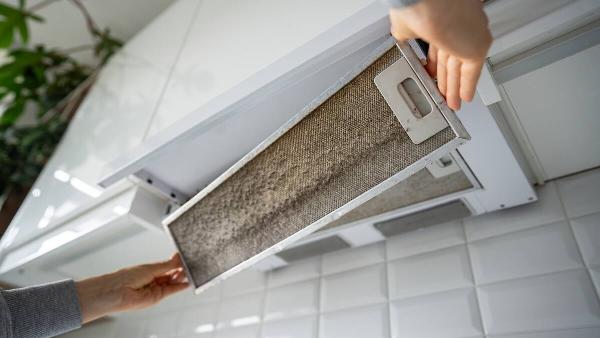 Hands removing dirty kitchen range hood filter. 