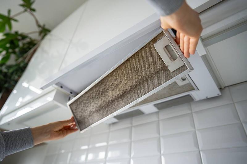 Hands removing dirty kitchen range hood filter. 