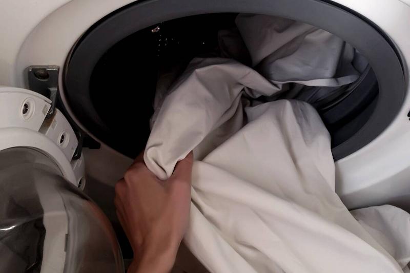 Hands putting shower curtain in washing machine. 