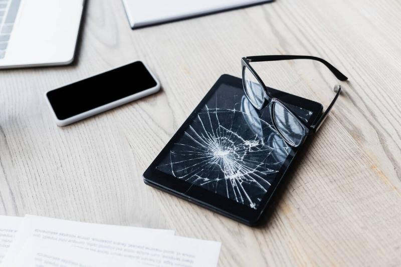 Eyeglasses on smashed digital tablet near documents and digital devices.