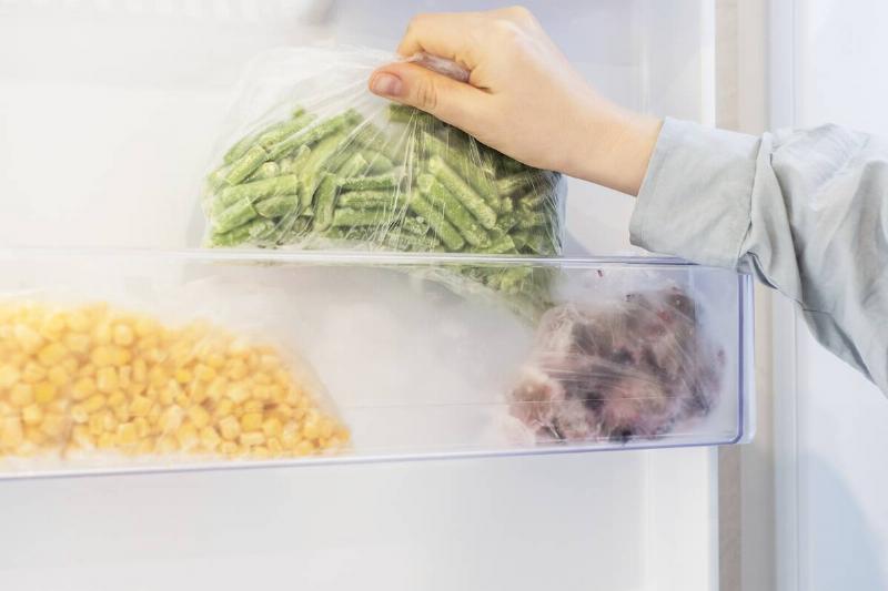 Woman pulling a bag of green beans from a freezer door shelf