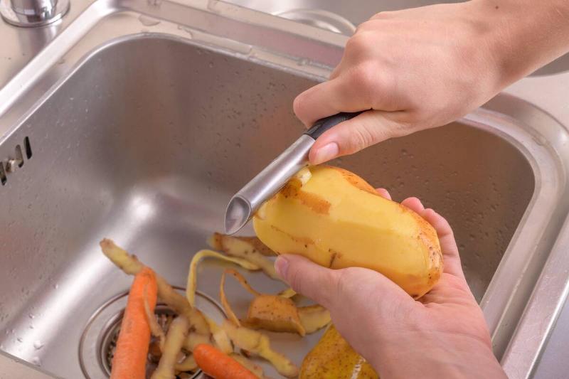 A person peeling potatoes into the kitchen sink. 