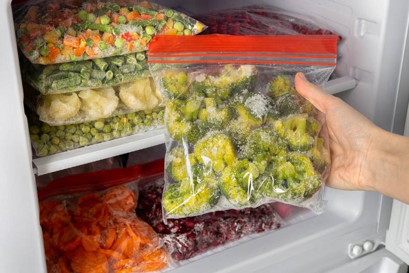 Person off-screen pulling a bag of broccoli out of a freezer