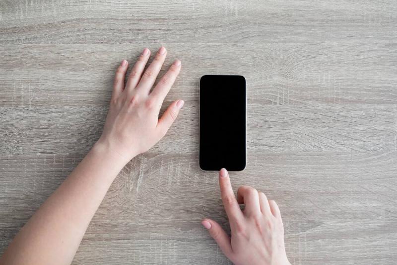 Hands touching a smartphone that has been turned off. 