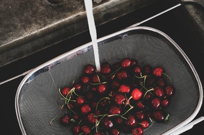 Fresh ripe garden harvest cherries being washed in strainer over kitchen sink.