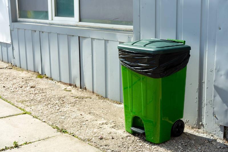 Green plastic garbage container standing in the street.