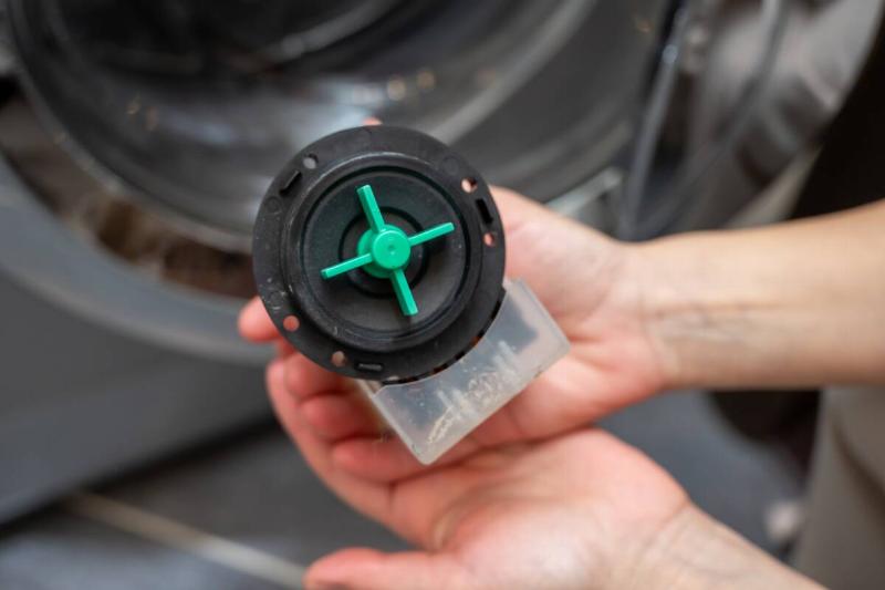 Close-up of a person holding a washing machine drain pump filter.