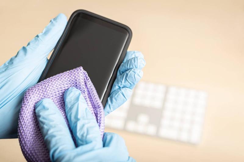 Hands in gloves use a microfiber cloth to clean a smartphone screen. 