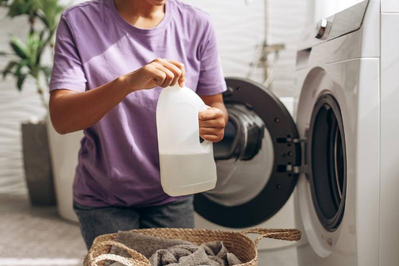 Woman putting vinegar in washing machine. 