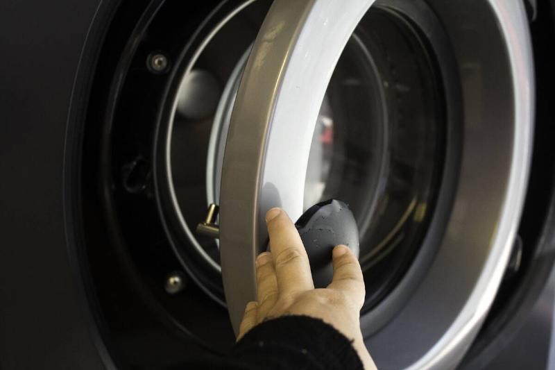 Hand opening the door of a washing machine. 