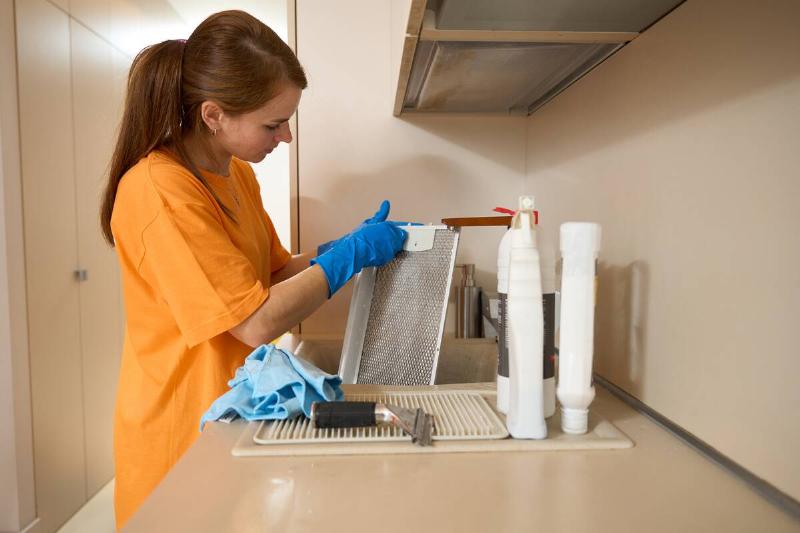 Woman cleaning kitchen range hood filter in sink. 