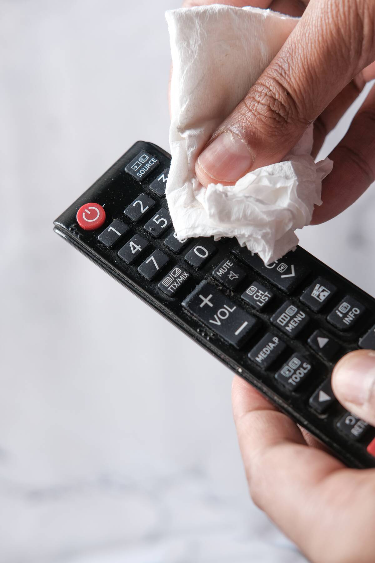 A hand cleaning a TV remote controller with disinfectant wet wipe.