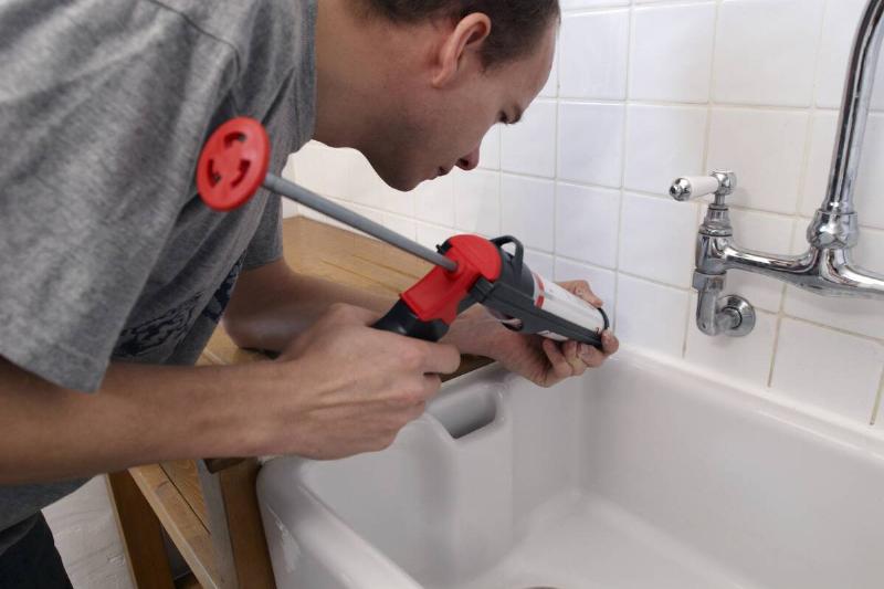 Man using a caulking gun around a kitchen sink