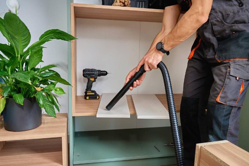 Man using vacuuming extension wand during shelf assembly. 