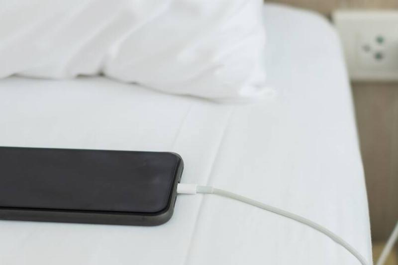 A phone charging and laying on a bed. 