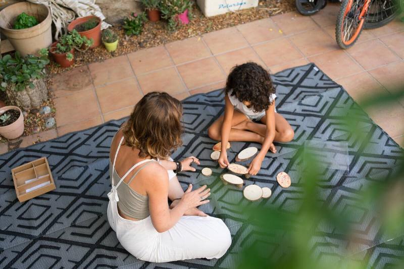 A woman and child sitting on a rug on a patio. 