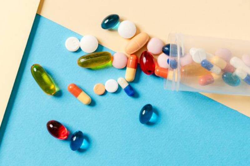 Overhead view of a scattered multicolored pills in a transparent jar lying on a colored background.