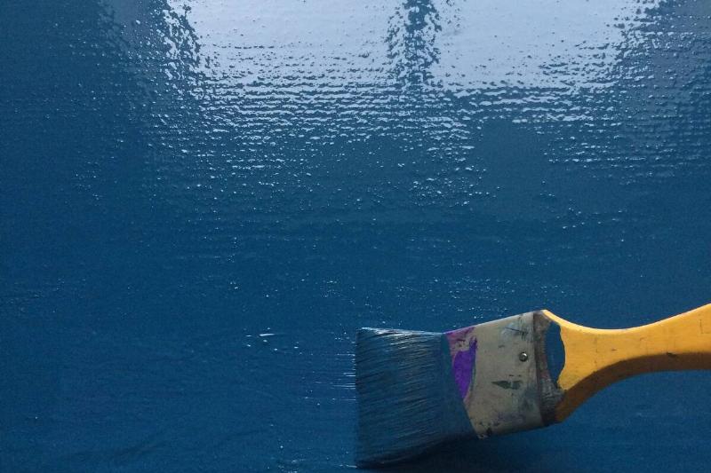 A paintbrush painting a glossy blue paint on a wall. 