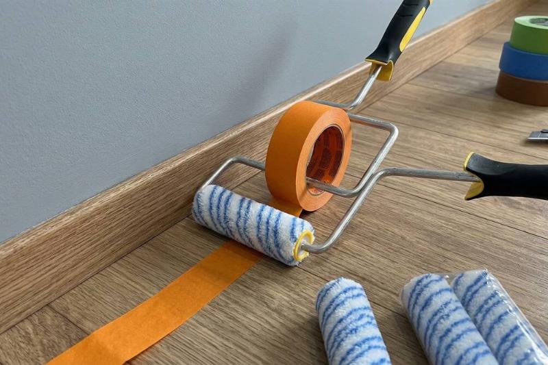 Painter's tape on a paint roller putting tape on the floor. 