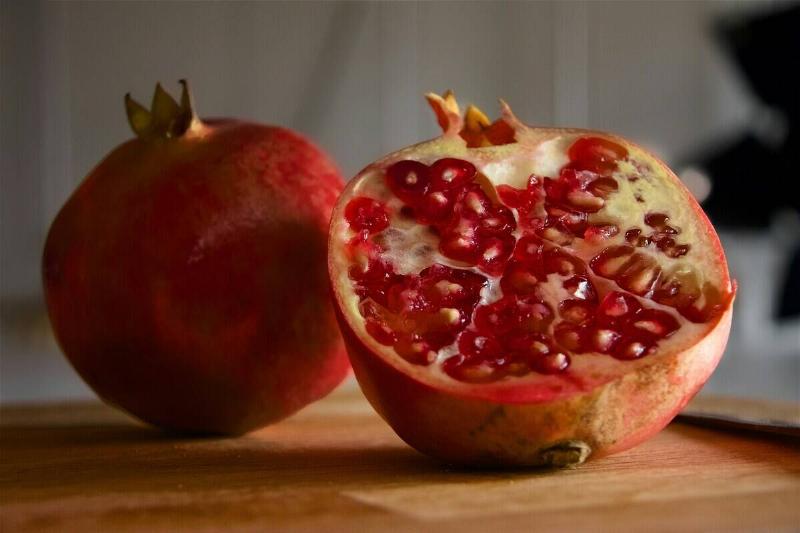 One whole pomegranate and half of another on a wooden cutting board