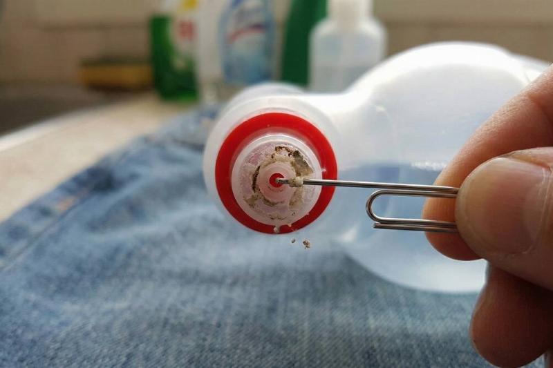 A paper clip being used to unplug a clogged spray nozzle.