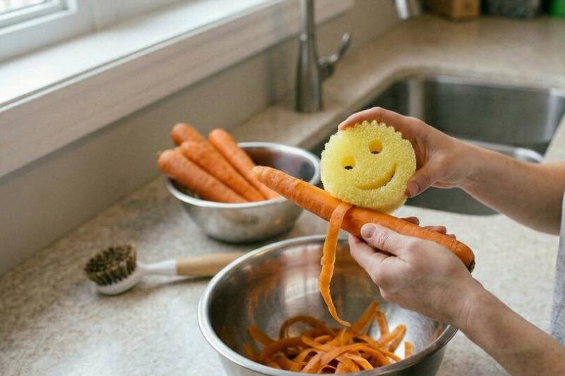 очистить скрабом папочки Женщина чистит овощи с помощью Scrub Daddy.