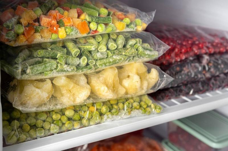 Frozen vegetables and fruit stacked in bags in a freezer