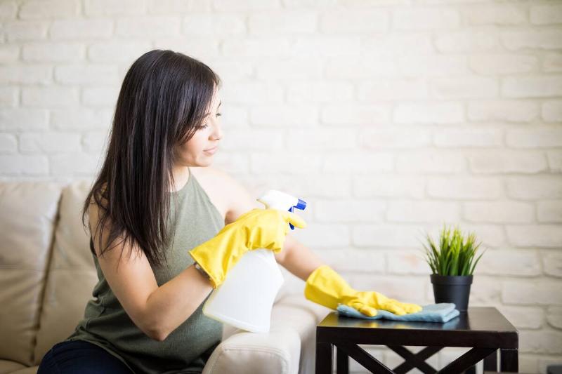 Woman sitting as she cleans a side table. 