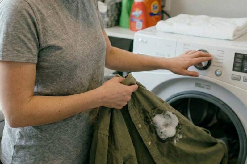 положить в стиральную машину Женщина кладет испачканную рубашку в стиральную машину.