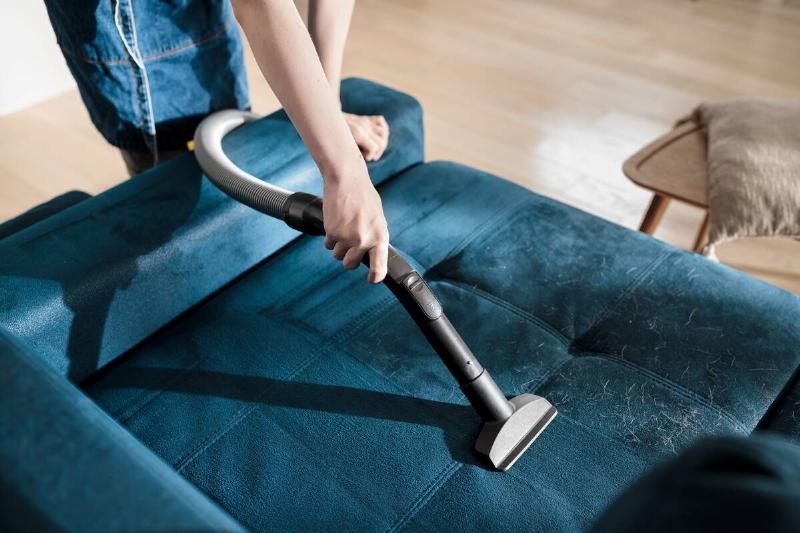Person cleaning couch with vacuum attachment.