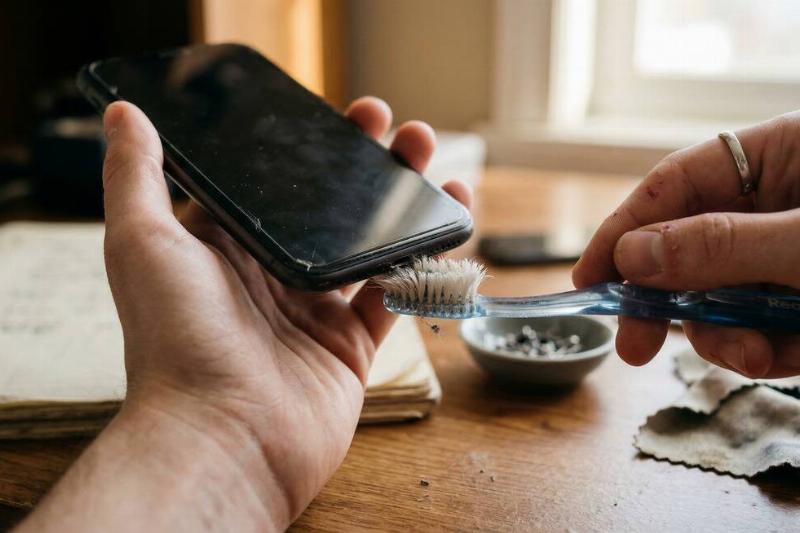 Cleaning the bottom of a smartphone with a toothbrush. 