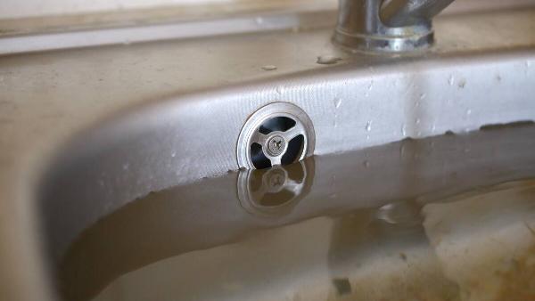 Stainless steel sink plug hole close up full of water and particles of food.