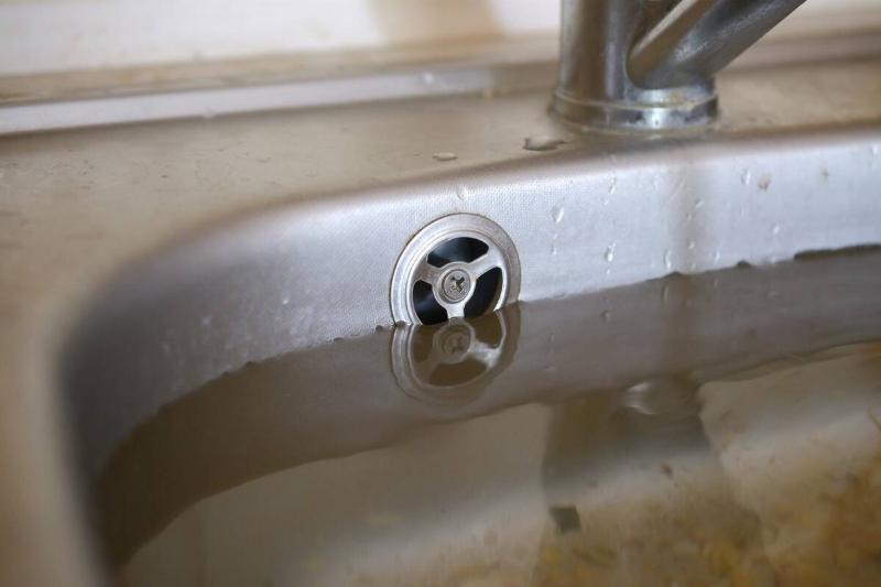 Stainless steel sink plug hole close up full of water and particles of food.