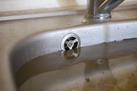 Stainless steel sink plug hole close up full of water and particles of food.