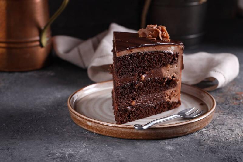 Slice of chocolate cake on a plate. A metal fork is also on the plate