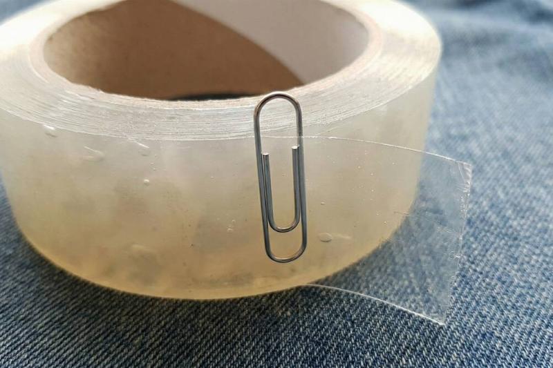 A paper clip showing the edge of a clear roll of tape. 