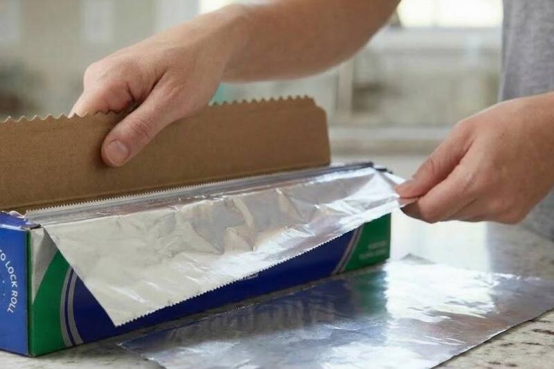 разрывая фольгу Рука вытаскивает алюминиевую фольгу и разрезает ее прямо.