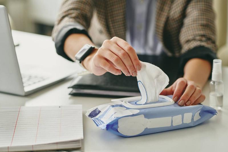 Person pulling disinfectant wipe out of package at desk. 