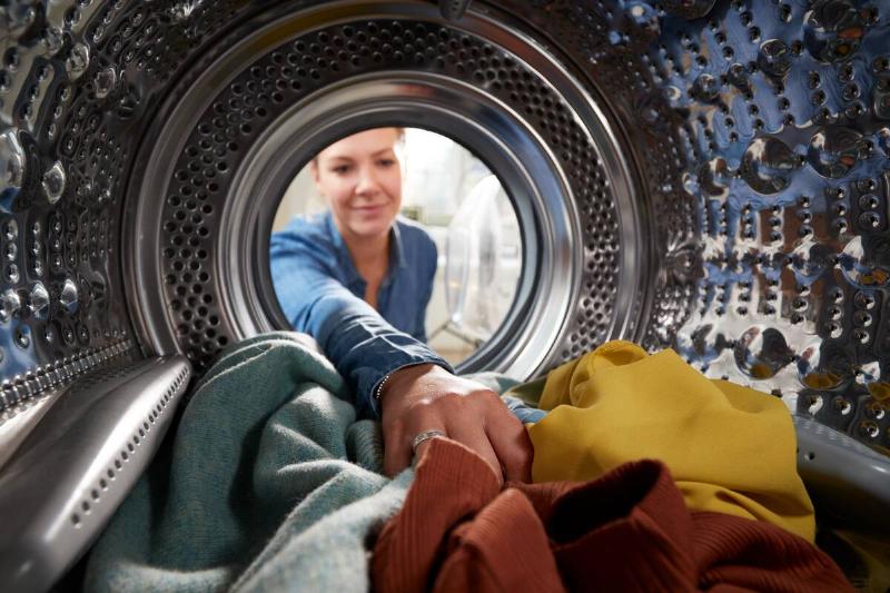 A woman reaching inside of dryer. 