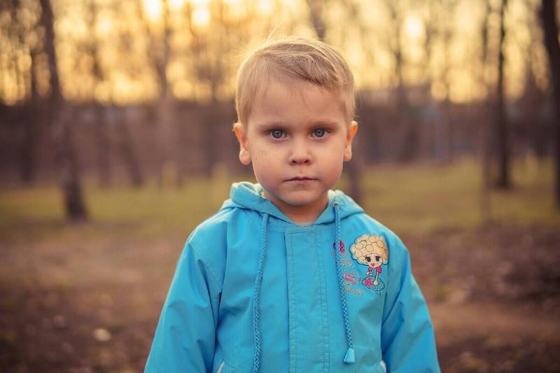 Child standing in a wooded area at sunset