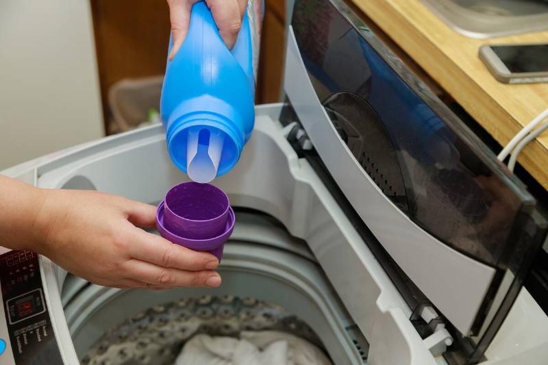 Person pouring detergent into washing machine. 