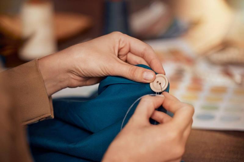 Person off-screen sewing a button to an item of clothing