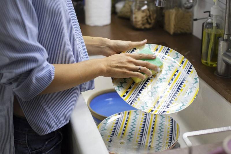 Hands washing dishes with sponge. 