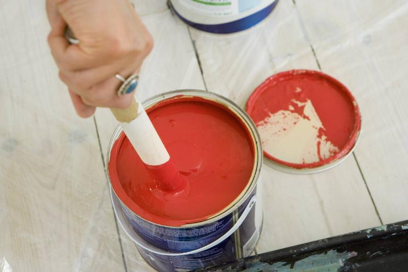 Person putting paintbrush in can of red paint. 