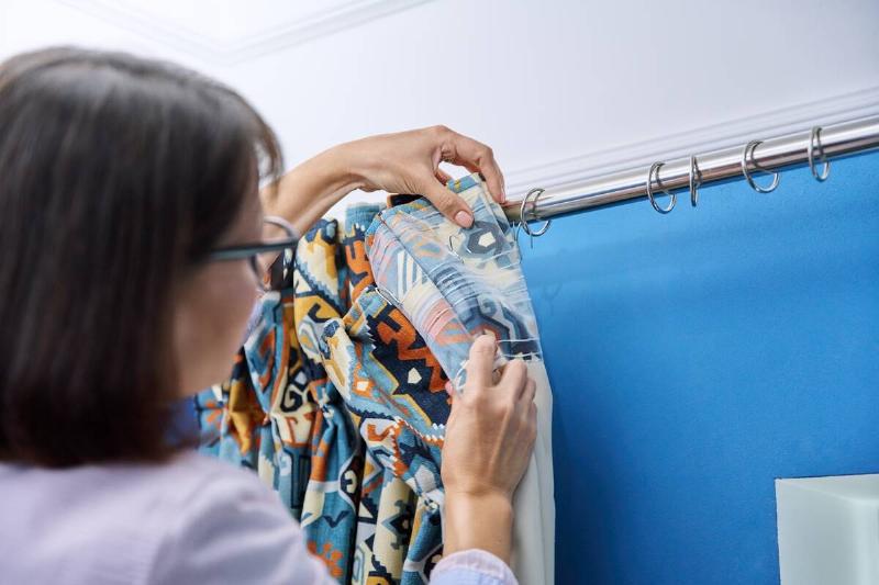 Woman hanging shower curtain back on hooks. 