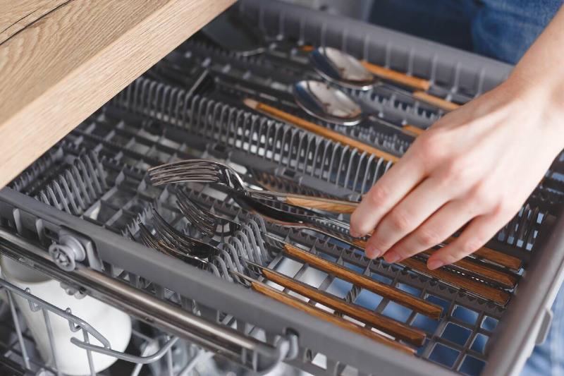 A person putting silverware in the top shelf of a dishwasher. 