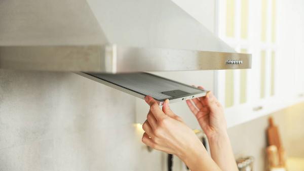 Hands removing filter from cooking range vet hood. 