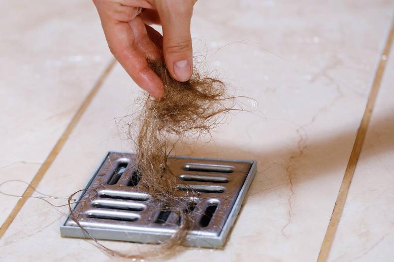 Woman removing hair clump from the shower drain.