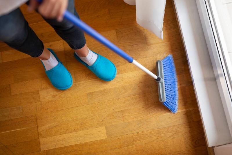 High angle view of female hands holding a broom and sweeping floor.